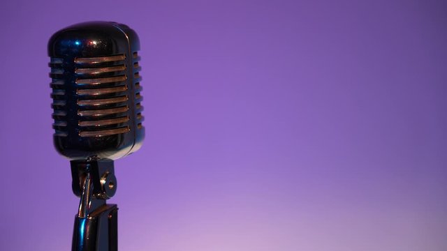Metallic concert vintage glare microphone for record or speak to audience on stage in dark empty retro club close up. Spotlights shine on a chrome mic on the left on purple color background. 