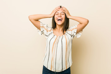 Fototapeta premium Young hispanic woman laughs joyfully keeping hands on head. Happiness concept.