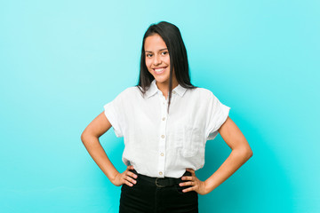 Young hispanic cool woman against a blue wall confident keeping hands on hips.