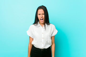 Fototapeta premium Young hispanic cool woman against a blue wall screaming very angry and aggressive.