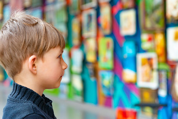 A surprised boy admires painting at an exhibition in an art gallery.