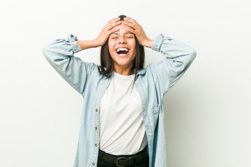 Young hispanic woman laughs joyfully keeping hands on head. Happiness concept.