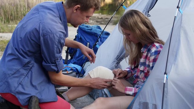 Young man bandaging up leg of his girlfriend on hike and she thanking him for help