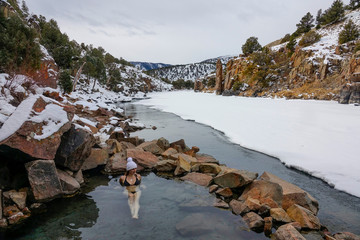 Young woman in bikini lies in Radium hot springs and observes snowy landscape