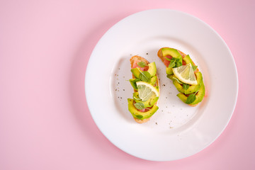 toasts with avocado salmon, basil leaves and a slice of lemon on a pink background. healthy breakfast concept.