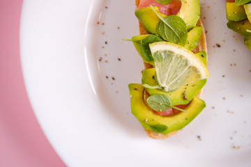 Fototapeta na wymiar toasts with avocado salmon, basil leaves and a slice of lemon on a pink background. healthy breakfast concept.