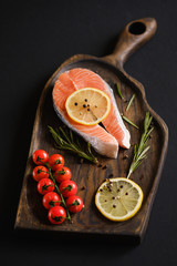 Raw, fresh salmon steak on a wooden board with lemon, rosemary and cherry tomatoes. Raw salmon, red fish. Cooking salmon, seafood. Healthy eating concept. Salmon and spices