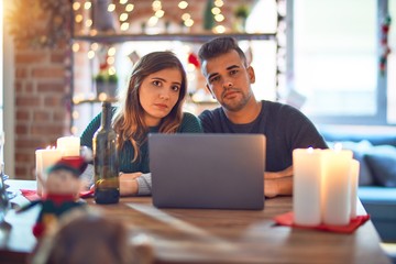 Young beautiful couple sitting using laptop around christmas decoration at home depressed and worry for distress, crying angry and afraid. Sad expression.