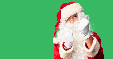 Middle age handsome man wearing Santa Claus costume and beard standing Ready to fight with fist defense gesture, angry and upset face, afraid of problem