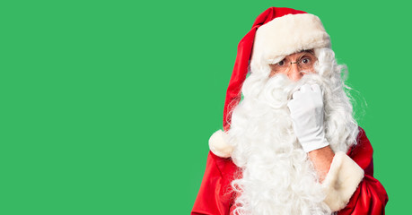 Middle age handsome man wearing Santa Claus costume and beard standing looking stressed and nervous with hands on mouth biting nails. Anxiety problem.