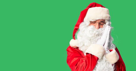 Middle age handsome man wearing Santa Claus costume and beard standing sleeping tired dreaming and posing with hands together while smiling with closed eyes.