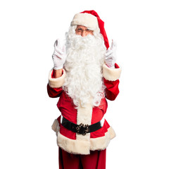 Middle age handsome man wearing Santa Claus costume and beard standing gesturing finger crossed smiling with hope and eyes closed. Luck and superstitious concept.