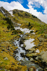 Mountain stream flows along the mountainside, snow. Nature background in spring or summer. Selective focus.