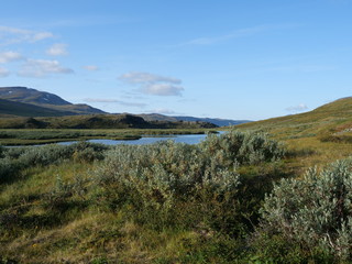 Lapland nature landscape with blue glacial river and Alesjaure STF Mountain cabin hut, birch tree forest, snow capped mountains and lonely red tent, Northern Sweden, at Kungsleden hiking trail. 