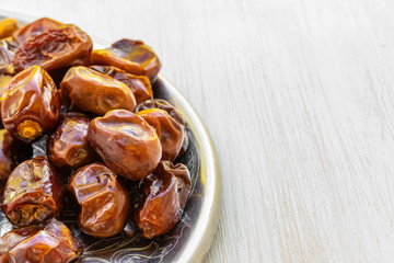 Dates lie on a silver tray on a white wooden background, side view from above