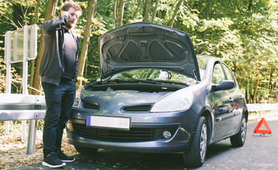 A broken car on the road, the driver holds an open hood and watches what has broken down, a roadside assistance is waiting