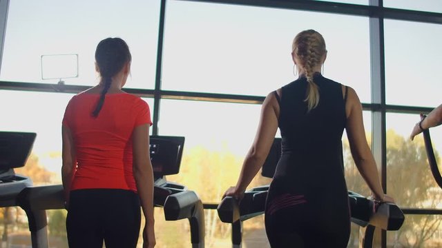 A group of people walking on treadmills near a large panoramic window. Group cardio workout. Start of fitness classes. Young beautiful women and men in sportswear in cardio fitness room