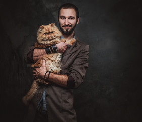 Portrait of happy smiling man with big and fluffy cat at dark photo studio.