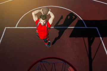 Young bearded guy athlete in a jump performs a slam dunk throwing a basketball into the basket. Basketball, sports lifestyle and sportswear. Competition, effort and determination. Jumping with ball. © Daniil