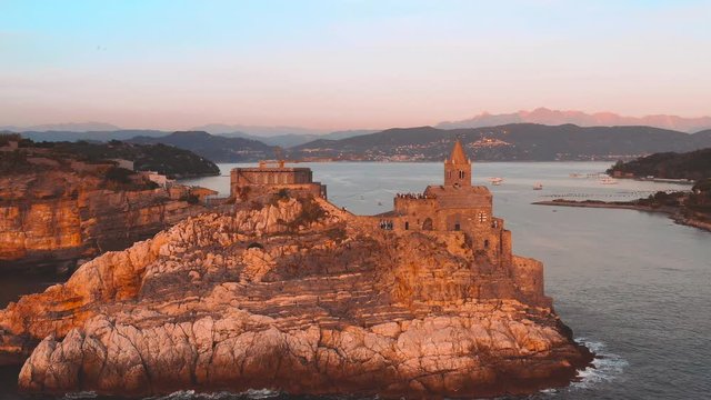 circular aerial tracking made with a drone flying over the church of San Pietro in Portovenere seen from the sea side during sunset