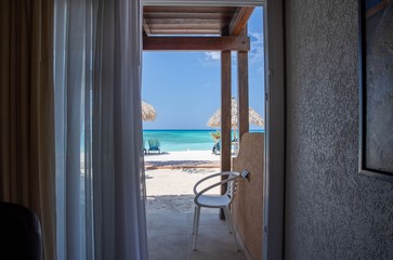 Gorgeous view on sandy beach and Atlantic Ocean from a room. Sun beds and umbrellas on turquoise water and blue sky background. Aruba island. 