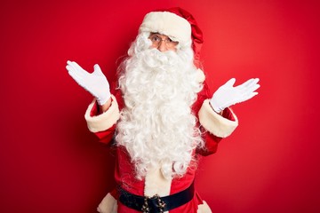 Middle age handsome man wearing Santa costume standing over isolated red background clueless and...