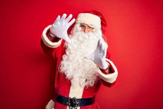 Middle age handsome man wearing Santa costume standing over isolated red background doing frame using hands palms and fingers, camera perspective