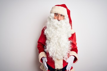 Middle age handsome man wearing Santa costume standing over isolated white background afraid and shocked with surprise and amazed expression, fear and excited face.