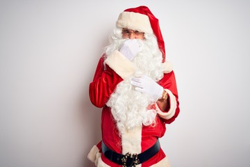 Middle age handsome man wearing Santa costume standing over isolated white background smelling something stinky and disgusting, intolerable smell, holding breath with fingers on nose. Bad smells 