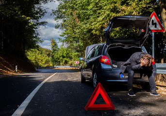 A broken car on the road, the driver holds an open hood and watches what has broken down, a roadside assistance is waiting
