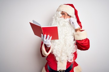 Middle age man wearing Santa Claus costume reading book over isolated white background mouth and...