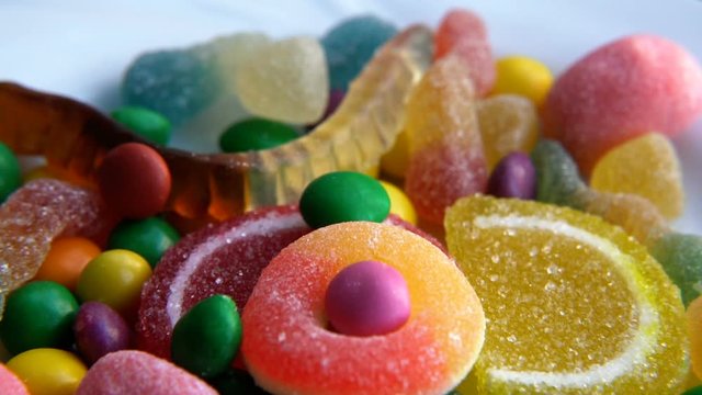Yummy multicolored fruity candies are rotating on a turntable and some candies are falling in slow motion