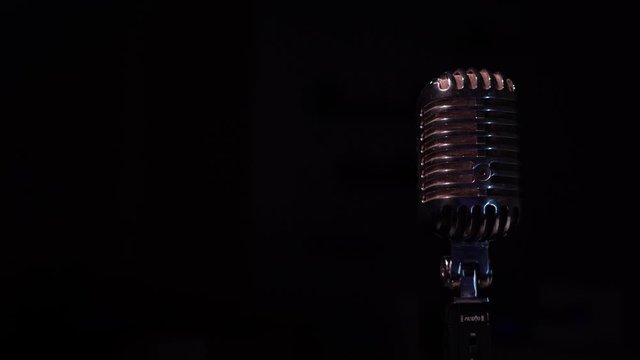 Red and white spotlights light on a chrome retro mic on the right on black background. Professional vintage glare microphone for record or speak to audience on stage in dark empty space close up. 