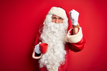 Obraz na płótnie Canvas Senior man wearing Santa Claus costume holding cup of coffee over isolated red background annoyed and frustrated shouting with anger, crazy and yelling with raised hand, anger concept
