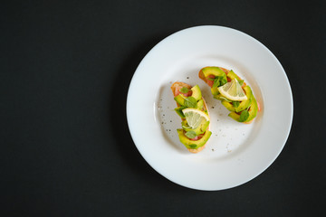 oasts with avocado salmon, basil leaves and a slice of lemon on a black background. healthy breakfast concept.