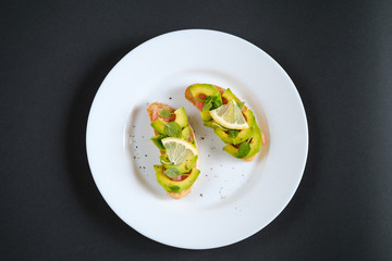 oasts with avocado salmon, basil leaves and a slice of lemon on a black background. healthy breakfast concept.