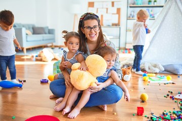 Fototapeta premium Beautiful teacher and group of toddlers playing around lots of toys at kindergarten