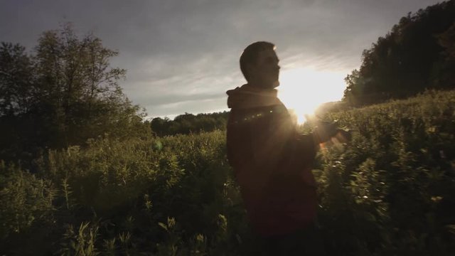 Rear view of a man running through wild green field with long grass. Stock footage. Camera follows runner in beautiful quiet fall, sunset meadow background.