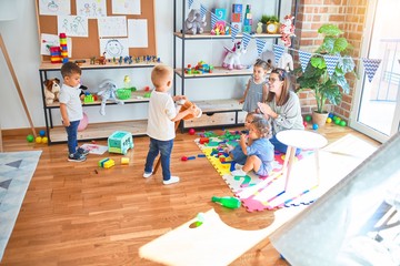 Beautiful teacher and group of toddlers playing around lots of toys at kindergarten