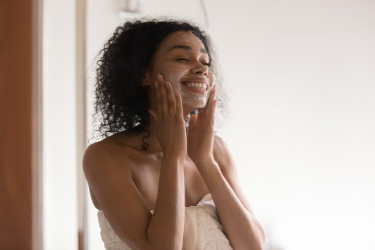 Happy African Americam Woman Applying Skincare Soothing Mask At Bathroom.