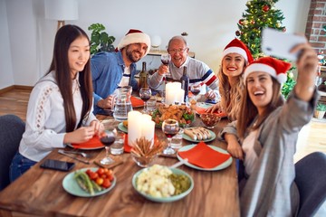 Beautiful family wearing santa claus hat meeting smiling happy and confident. Eating roasted turkey make selfie by smartphone celebrating Christmas at home