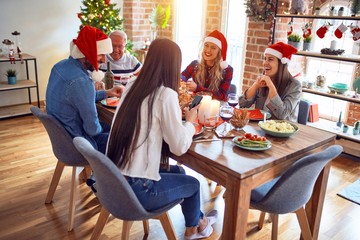 Beautiful family wearing santa claus hat meeting smiling happy and confident. Eating roasted turkey using smartphone celebrating Christmas at home