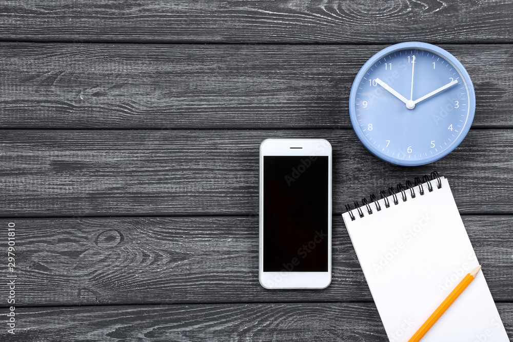 Poster smartphone with round clock and notepad on black wooden table