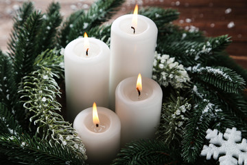 Christmas candles with fir tree branches and snowflakes on brown wooden table