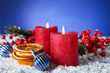 Christmas candles with dry oranges, baubles and red berries on blue background