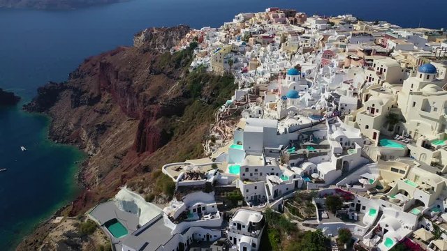 Aerial drone video of famous whitewashed and colourful at the same time picturesque village of Oia built on a cliff, Santorini island, Cyclades, Greece
