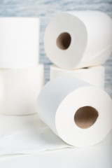 A pile of toilet paper rolls on a white table on a background of blue wall texture. The concept of using natural materials for hygiene products