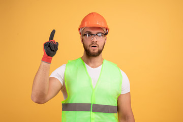 Positive repairman lifted his thumb up, he had the idea,wears orange protective construction helmet, reflective waistcoat and protective glasses, ready for house renovation.