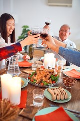 Beautiful group of people meeting smiling happy and confident. Eating roasted turkey and toasting with cup of wine celebrating Thanksgiving Day at home