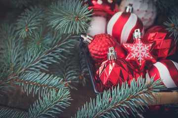 Christmas red and white glass toys in the basket with fir tree branches background, selective focus
